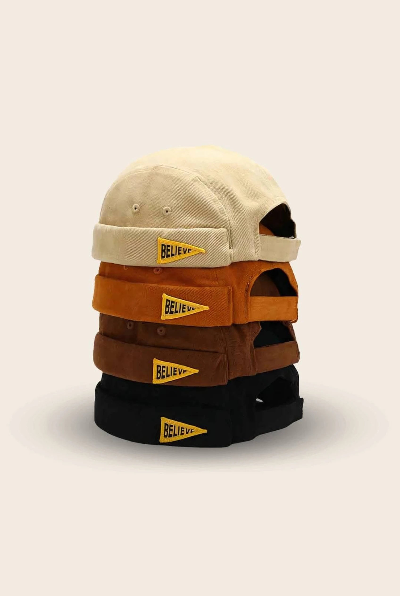 Les 4 coloris du bonnet docker Believe empilés : beige, orange, marron et noir