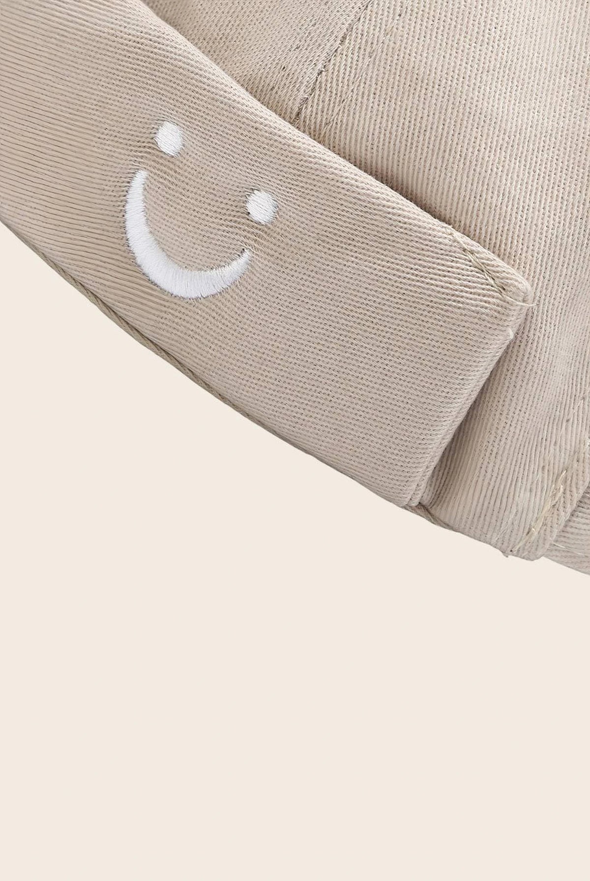 Gros plan sur le patch smiley brodé du bonnet docker beige